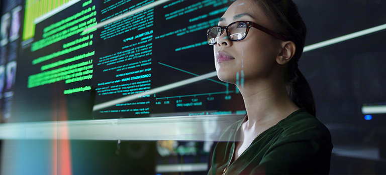 Person working in front of a large screen displaying green code and technical data, representing IT and software development.